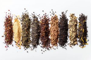 Assorted loose leaf teas and spices on white background.